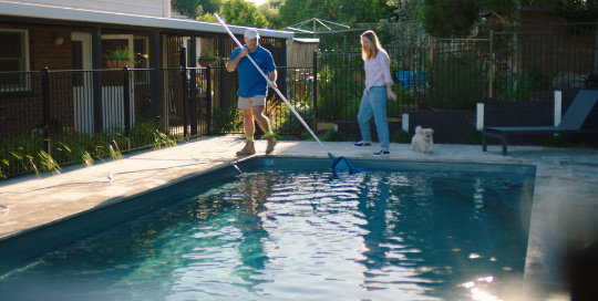 Couple cleaning pool with dog.